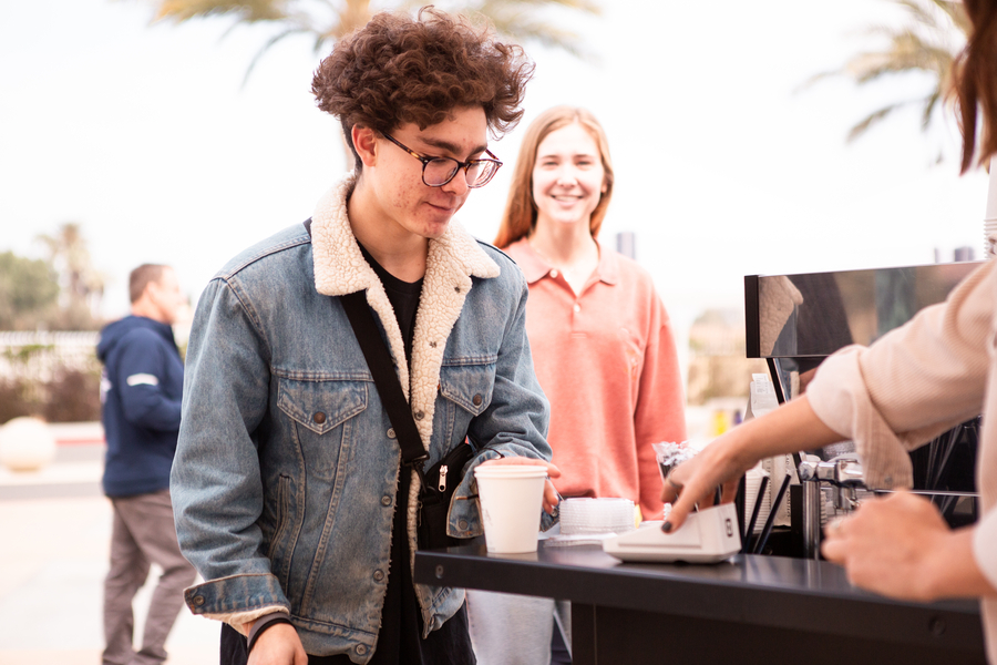 A CBU student buying a coffee at an outdoor coffee cart